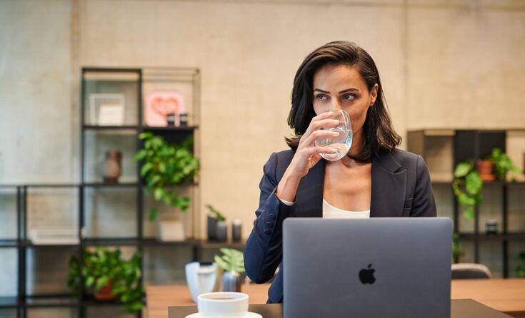 Kollegin trinkt Wasser vor ihrem PC