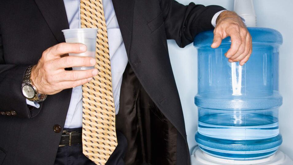 Ein Geschäftsmann mit gelber Krawatte steht an einem Wasserspender