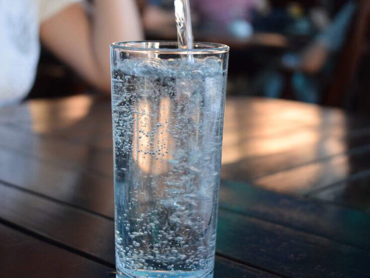 Ein sprudelndes Wasserglas was auf einem Holztisch steht