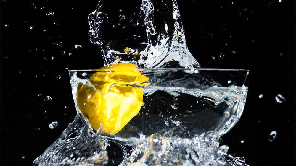Zitrone fällt in gefuelltes Wasserglas
