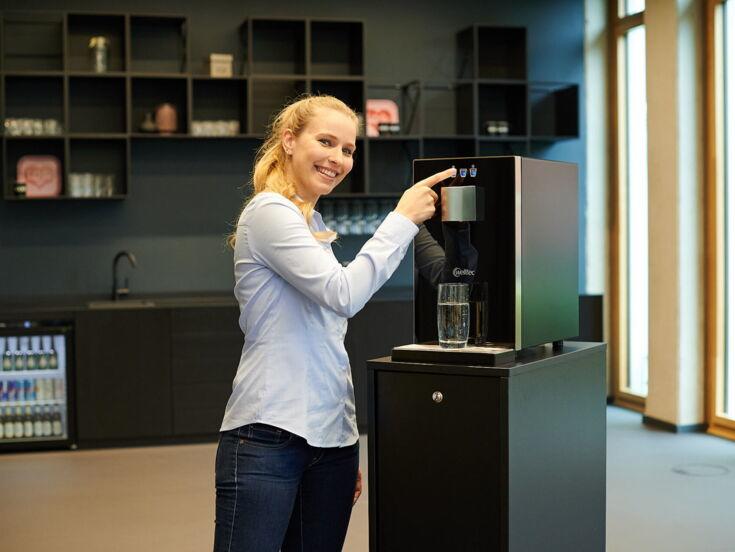 Junge Frau zieht sich ein Glas Wasser aus dem Wasserspender