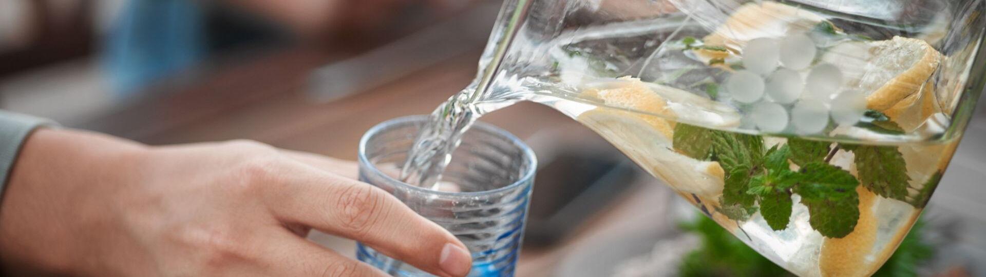 Wasser aus einer Wasserkaraffe wird in Wasserglas gegossen