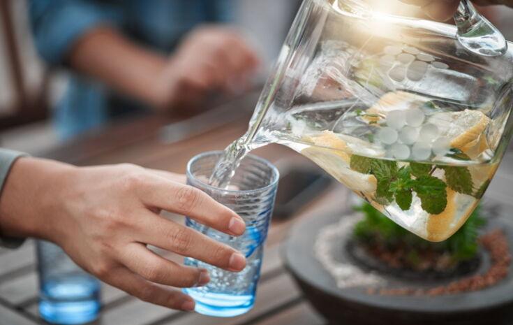 Wasser aus einer Wasserkaraffe wird in Wasserglas gegossen