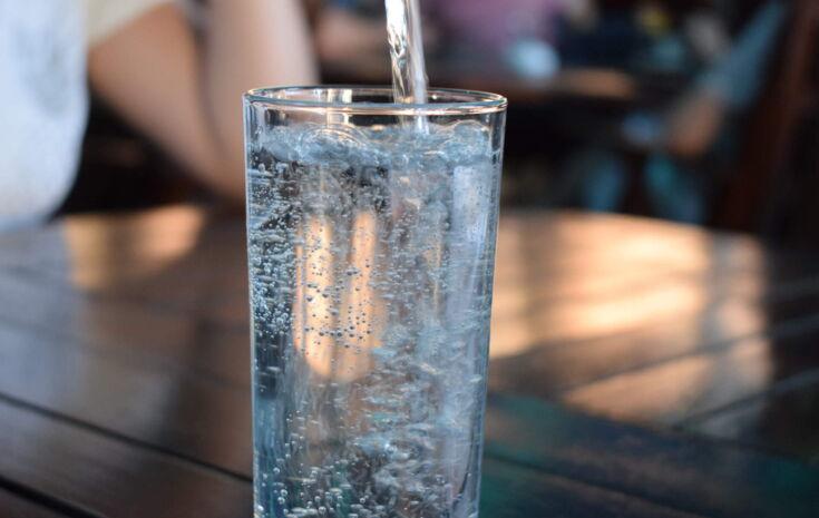 Ein sprudelndes Wasserglas was auf einem Holztisch steht