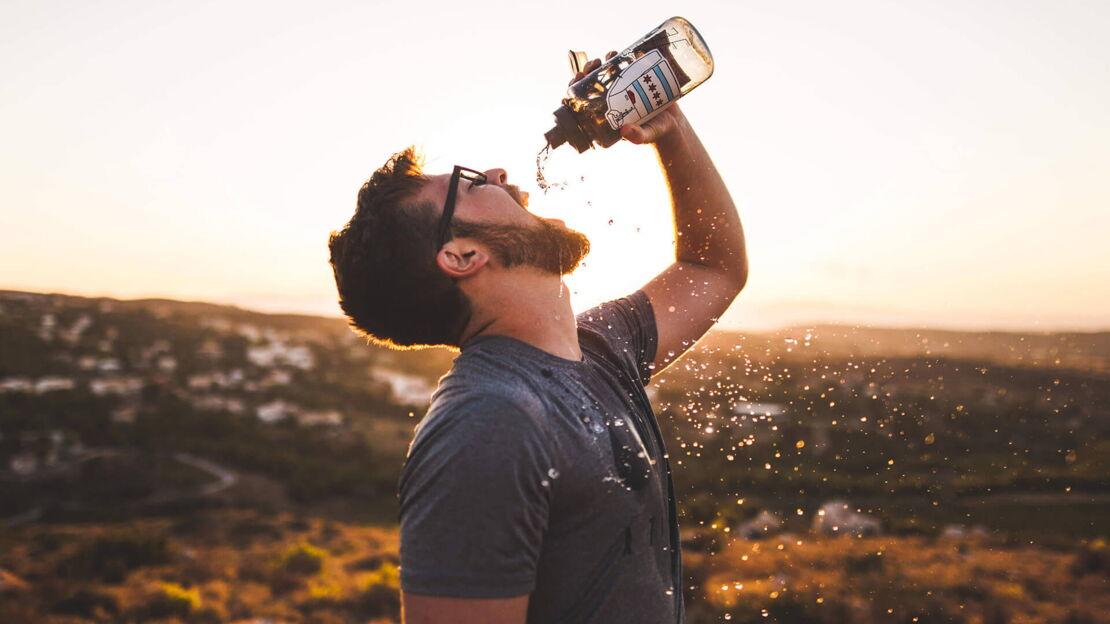 Mann trinkt Wasser aus Flasche in Natur