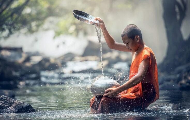 Ein Junge sitzt in einem Fluss und gießt Wasser auf einen Topf