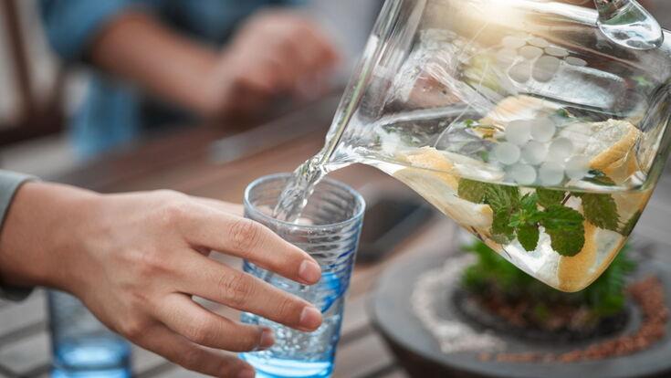 Wasser aus einer Wasserkaraffe wird in Wasserglas gegossen