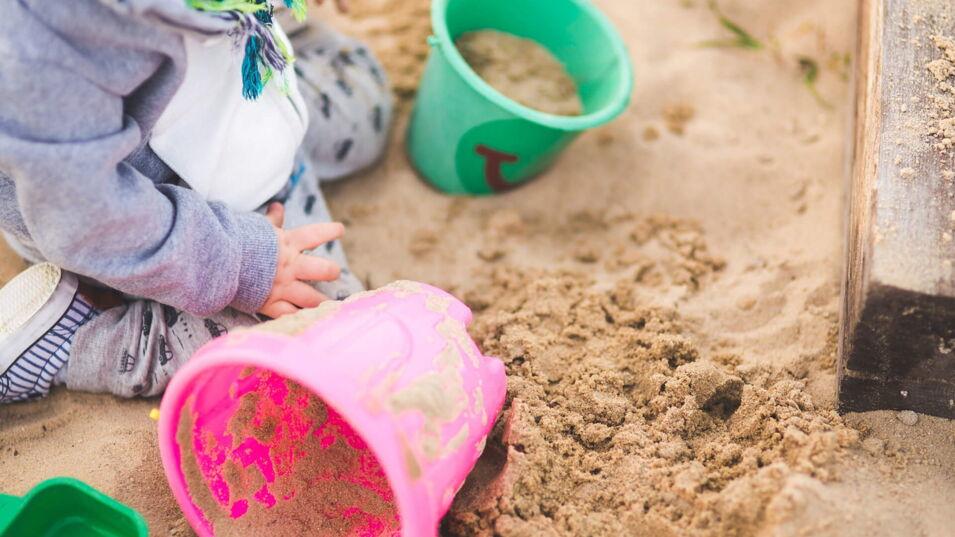 Kleines Kind sitzt in einem Sandkasten und spielt