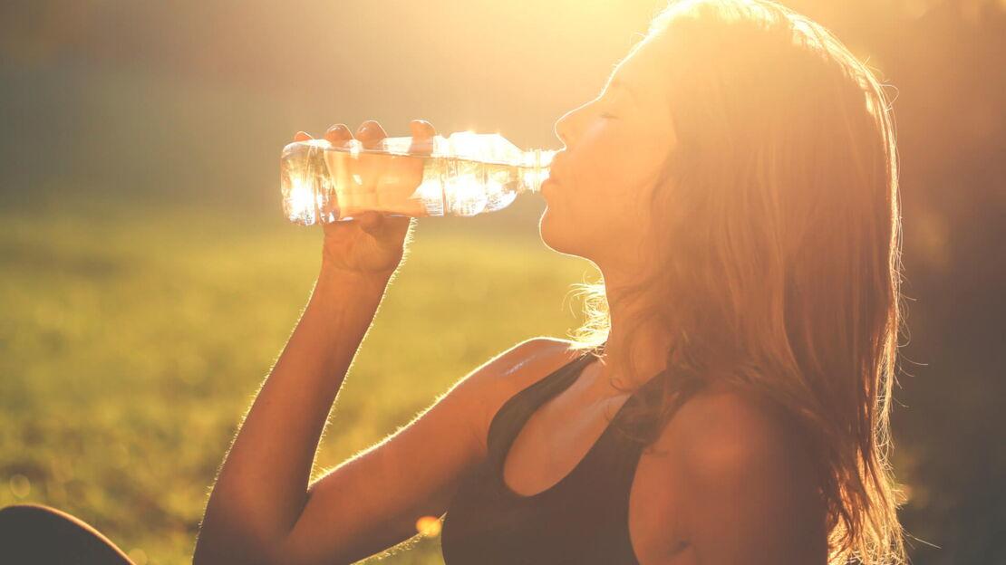 Eine junge Frau sitzt auf einer Wiese und trinkt Wasser