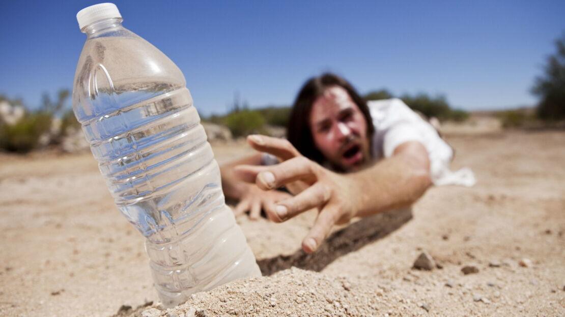 Mann greift nach Wasserflasche im Sand