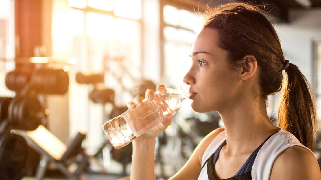 Sportliche junge Frau trinkt Wasser in einem Fittnesstudio