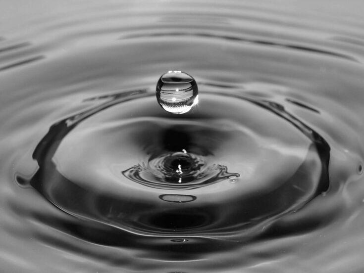 Wassertropfen auf Wasseroberflaeche in dunkler Optik