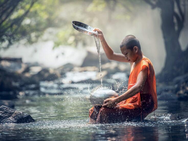 Ein Junge sitzt in einem Fluss und gießt Wasser auf einen Topf