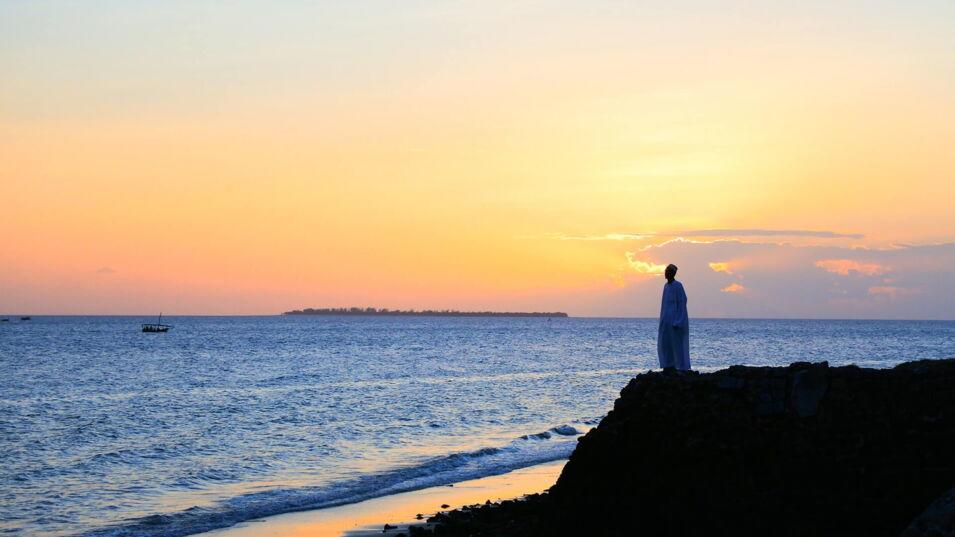 Ein Mann steht auf einer Düne und schaut auf das Meer bei Sonnenuntergang