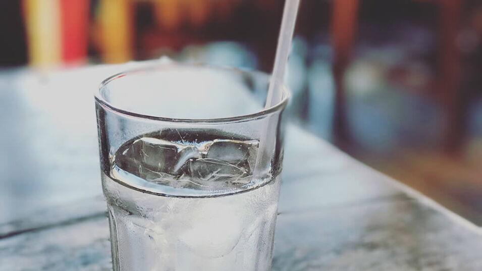Ein Glas Wasser mit Eiswürfeln steht auf einem Holztisch
