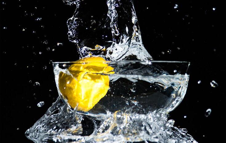 Zitrone fällt in gefuelltes Wasserglas