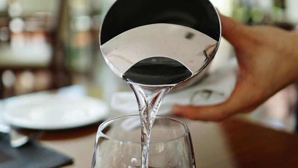 Wasserbedienung schenkt Wasser in ein Glas